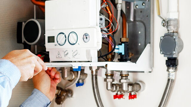 Eine männliche Person verwendet einen Schraubenzieher an einem geöffneten gasbetriebenen Durchlauferhitzer.