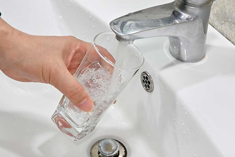 In ein Glas fließt Wasser aus einem Wasserhahn.