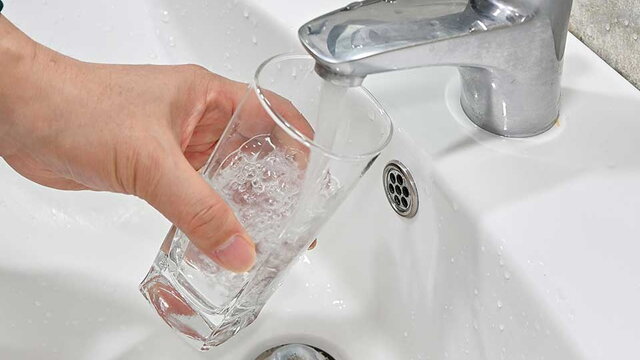 In ein Glas fließt Wasser aus einem Wasserhahn.